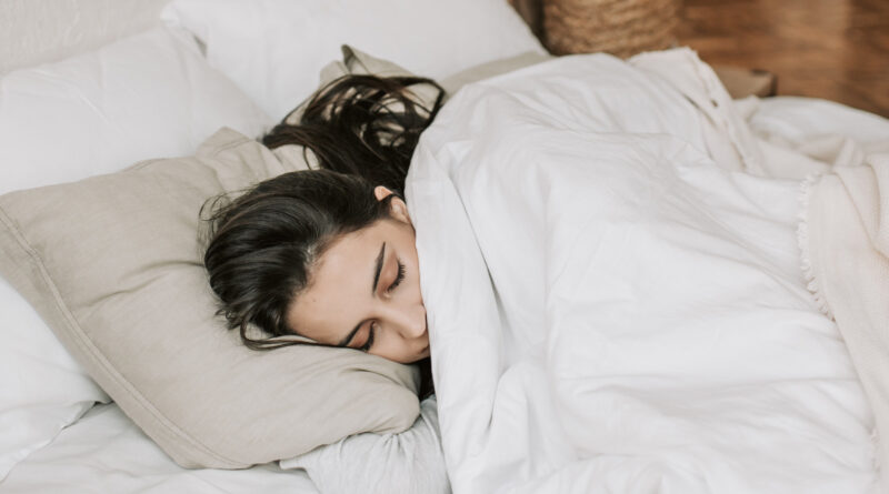 Brunette woman sleeping on beige pillow and white duvet