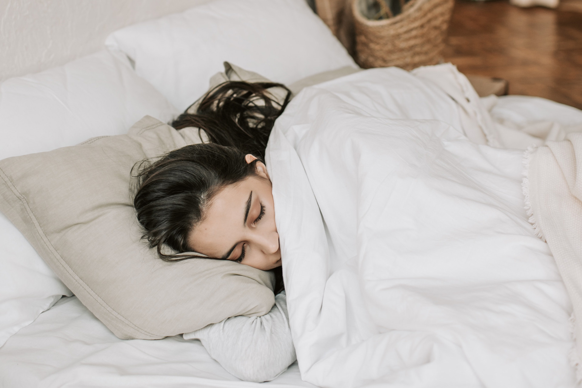 Brunette woman sleeping on beige pillow and white duvet